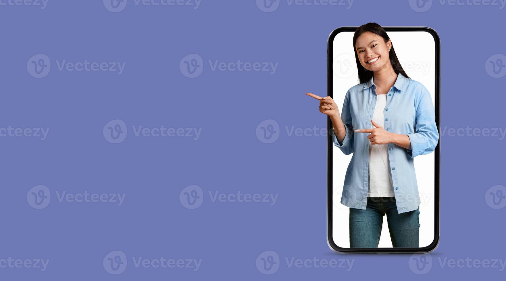 A joyful woman stands in front of a large smartphone display, interacting with a social media application. She points enthusiastically, highlighting modern communication technology. photo