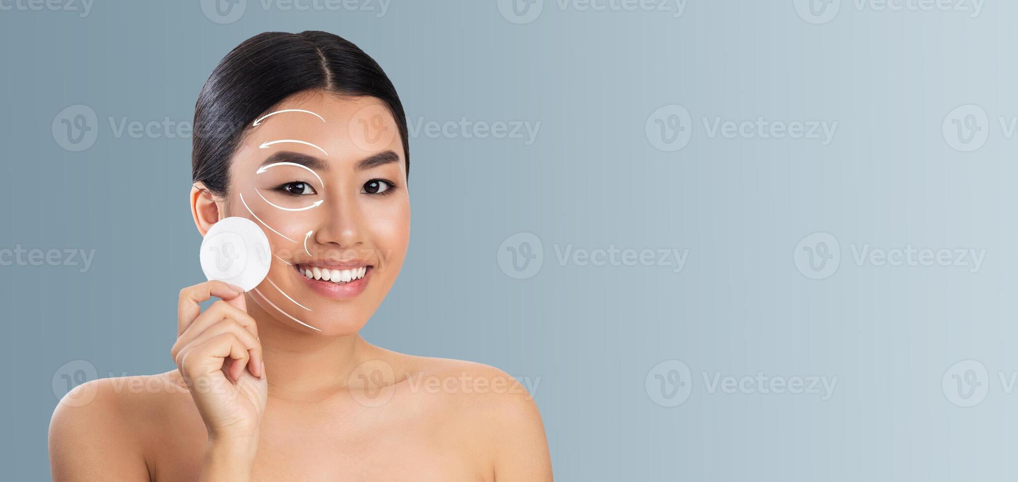 Asian woman enjoys her skincare routine, smiling while holding a cotton pad. The soft background enhances the focus on her glowing skin and joyful expression, creating a calming atmosphere. photo