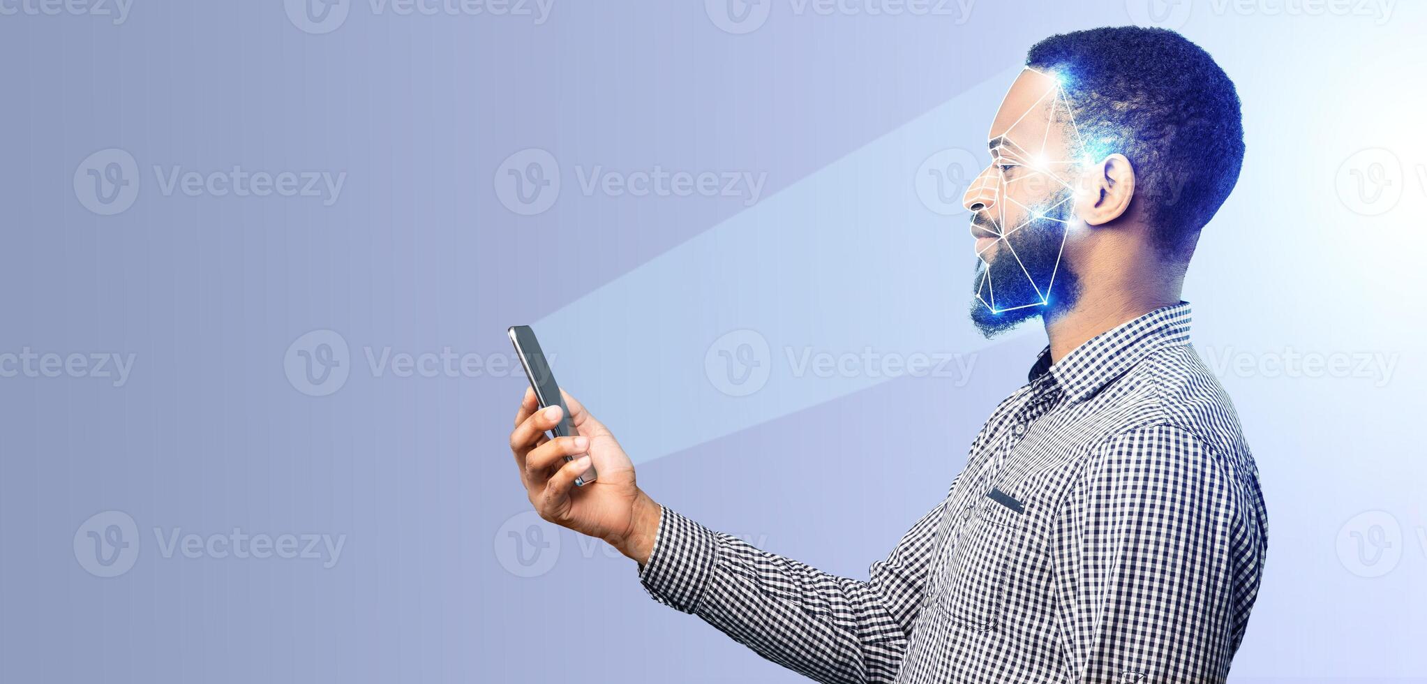 A man stands in an isolated setting, using facial recognition technology on his smartphone. He gazes at the screen, highlighting advancements in identification and security. photo