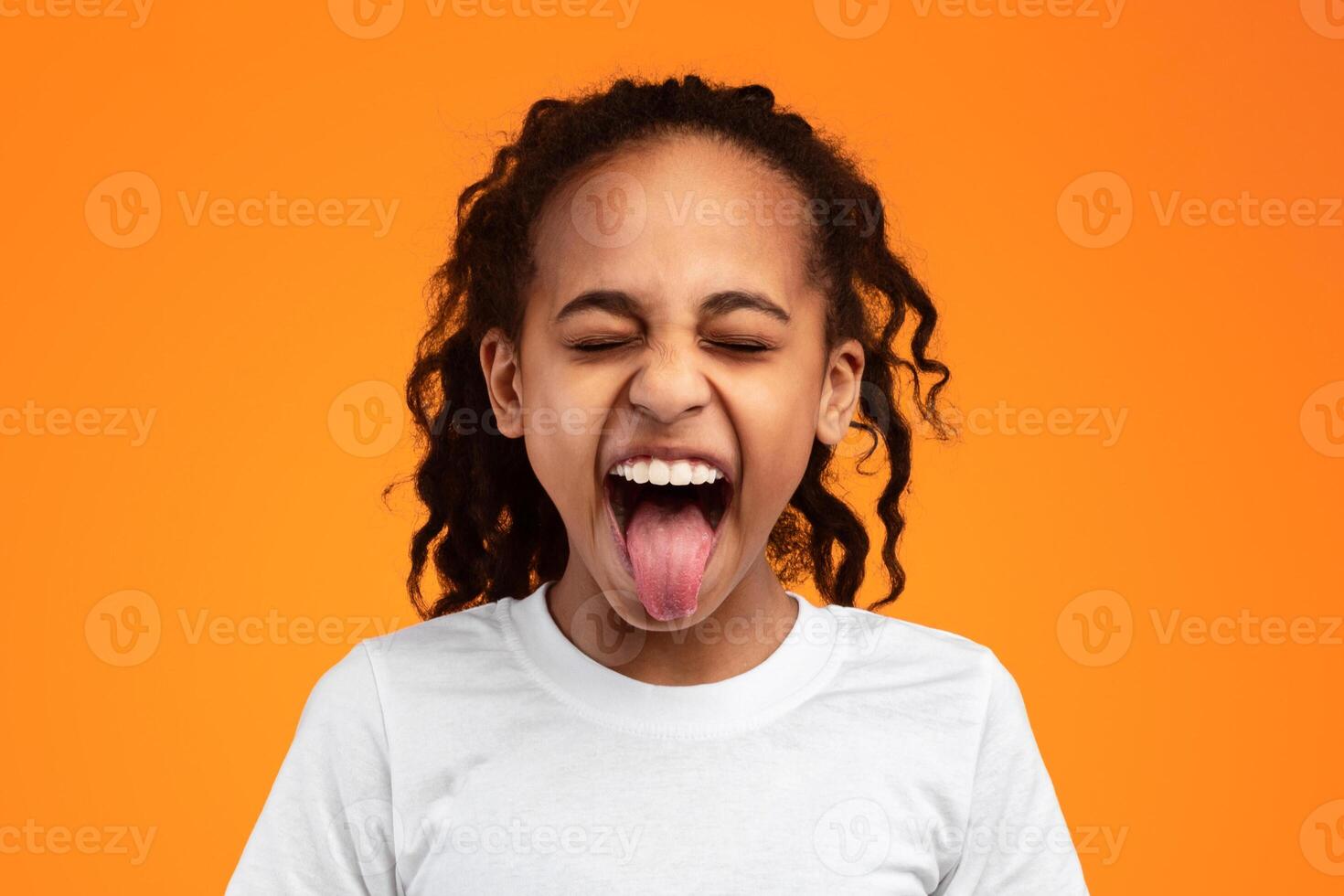 Human Emotions, Reactions And Attitude Concept. Closeup portrait of African American girl showing sticking out her tongue at camera, playing and having fun. Goofy kid fooling around photo