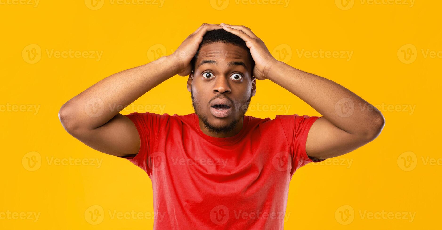 Omg. Black Man Touching Head In Shock Looking At Camera In Surprise Posing Standing Over Yellow Background In Studio, Wearing Bright T-Shirt. Shocking News, Human Emotions Concept photo