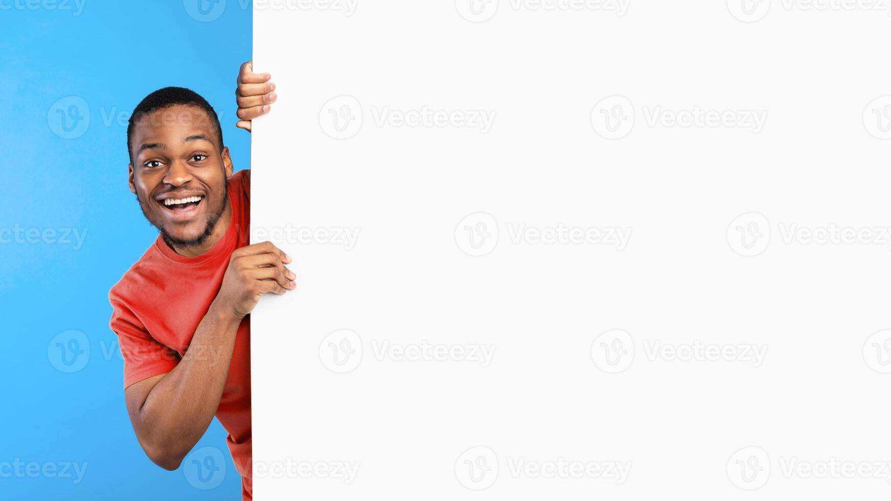 Great Offer Advertisement. Excited African American Man Posing With Big White Poster Looking Smiling To Camera Over Blue Studio Background. Bright Ad Banner With Copy Space. Mockup, Panorama photo