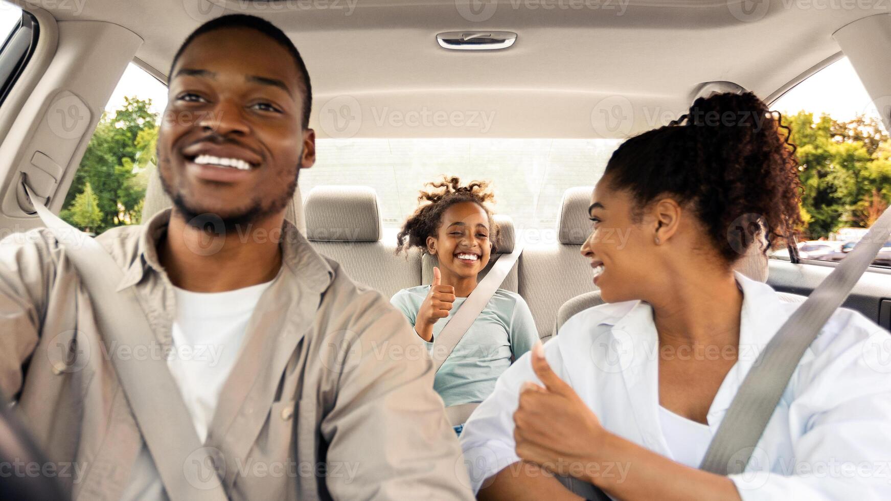 New Car. Happy Black Family Of Three Driving Own Car Gesturing Thumbs Up Approving Vehicle Sitting In Automobile. Road Trip On Vacation Concept. Selective Focus photo