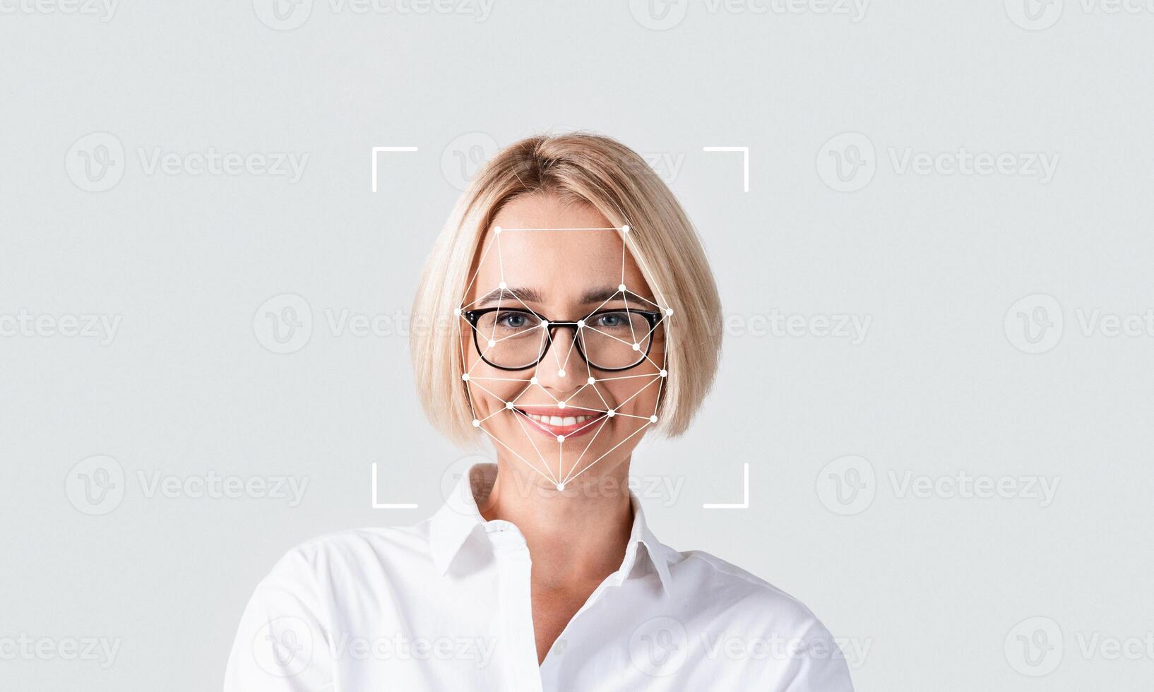 A person with short blonde hair wears glasses while smiling confidently. The focus is on facial recognition technology, highlighting features and characteristics in a neutral setting. photo