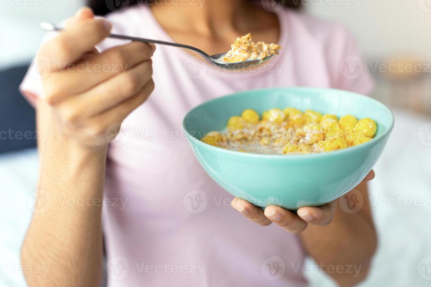Healthy slimming diet concept. Cropped view of Indian lady with bowl of cereal at home, closeup. Unrecognizable Hindu woman having balanced breakfast, enjoying cornflakes with milk photo