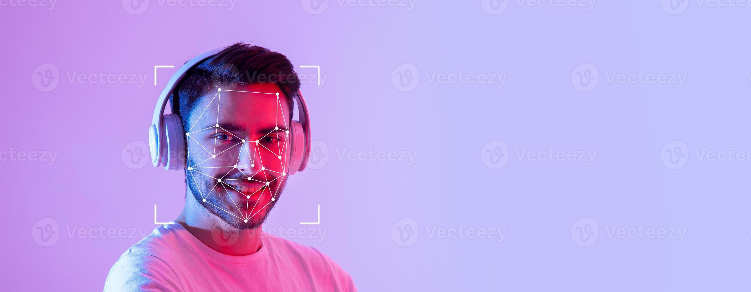 A young man smiles while wearing headphones, showcasing facial recognition technology on his face. The background is a vibrant purple, enhancing the tech-focused atmosphere. photo