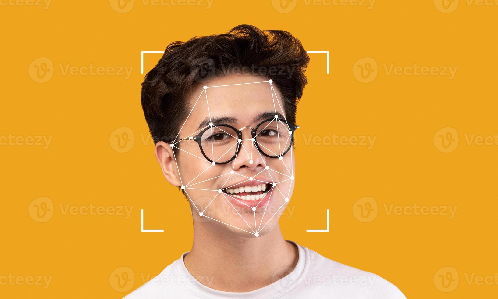 A young man with spectacles smiles brightly against a vibrant yellow background. Facial recognition markers are displayed over his face, illustrating technological identification processes. photo