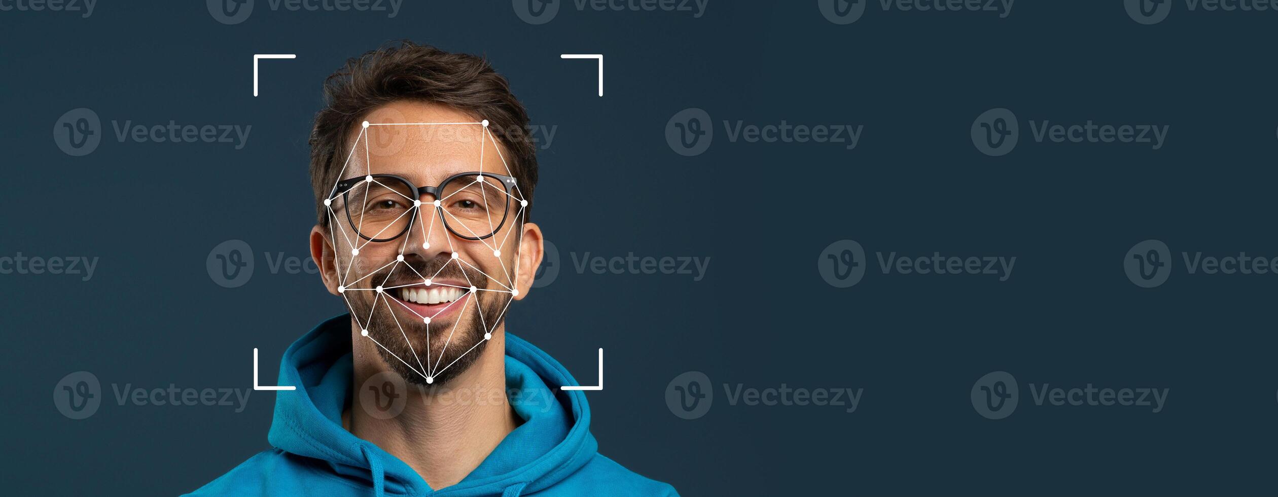 A smiling man wears glasses and a hoodie while facial recognition technology overlays a geometric pattern on his face. The background is a solid color, emphasizing facial identification. photo