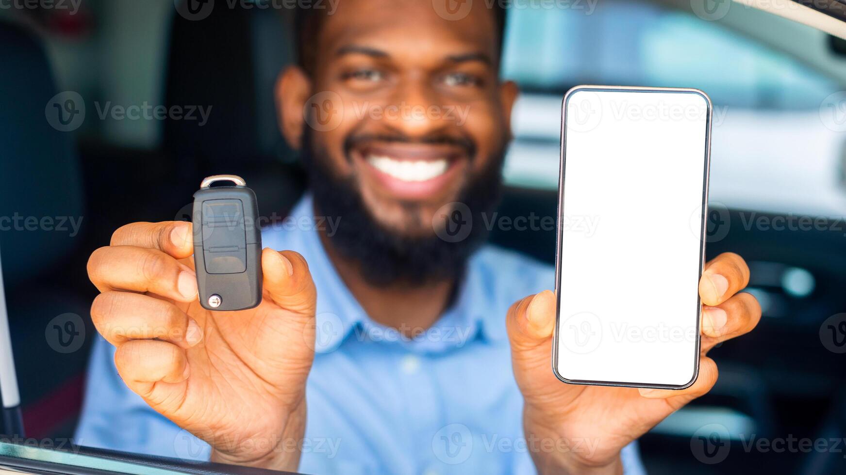 Car Renting App. Happy Black Man Showing Key And Smartphone With Blank White Screen Through Window While Sitting In His Automobile In Dealership Center Or Rental Office, Closeup Shot, Mockup photo