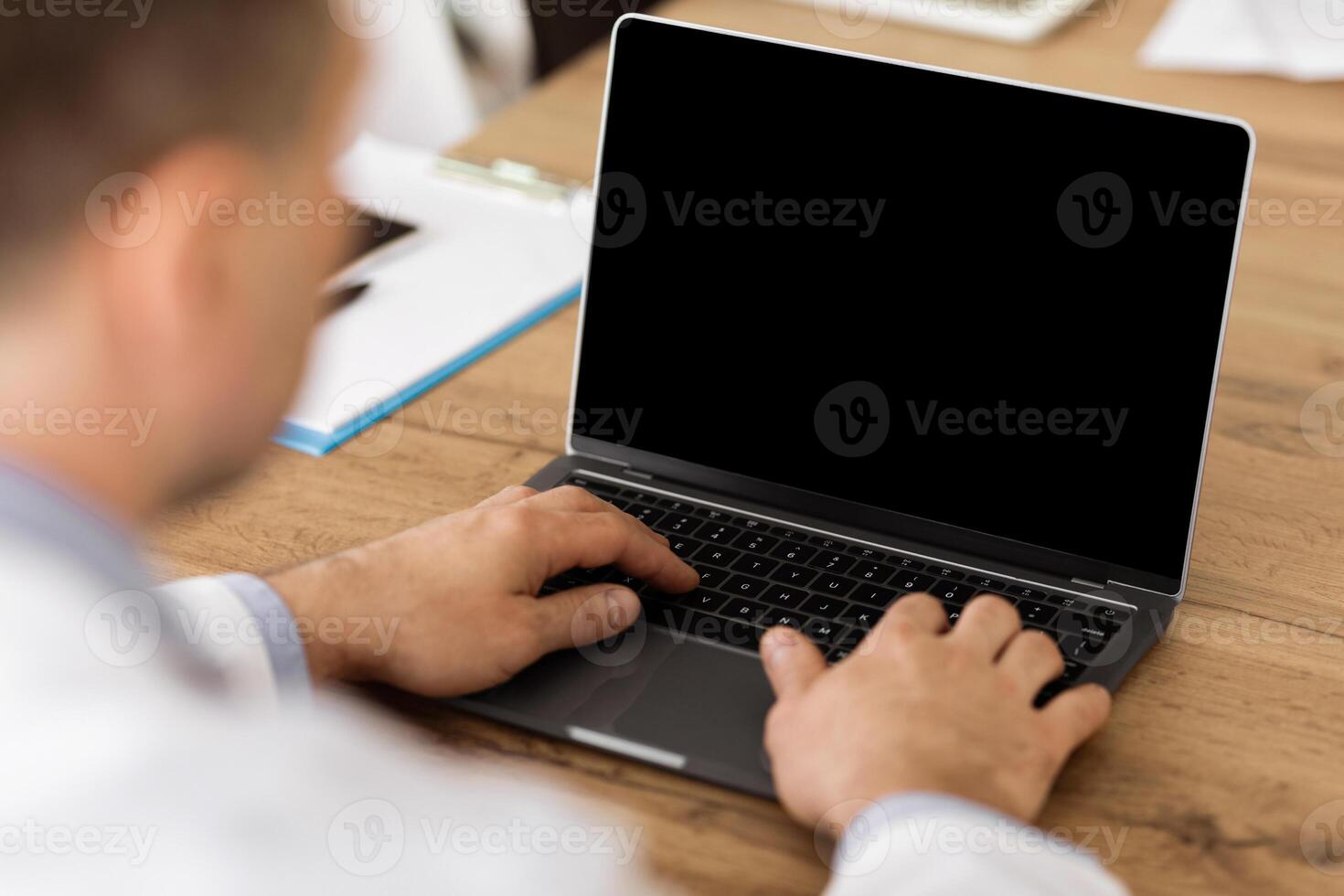 Lifestyle And Modern Technology Concept. Man using laptop with blank black screen for mock up template, sitting at wooden desk, view over the shoulder, back shot. Person working on notebook photo