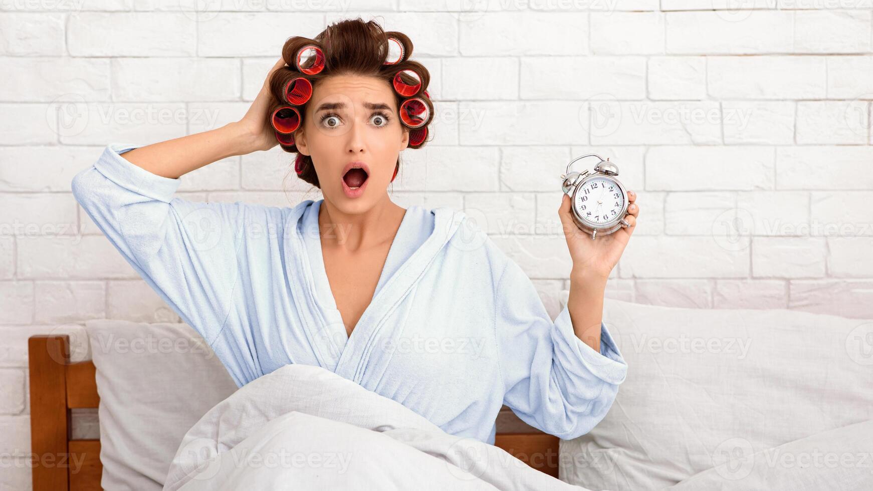 Oversleeping. Shocked Overslept Woman Holding Alarm Clock Being Late For Work Sitting In Bed At Home In The Morning, Looking At Camera. Deadline, Not In Time Concept. Panorama photo