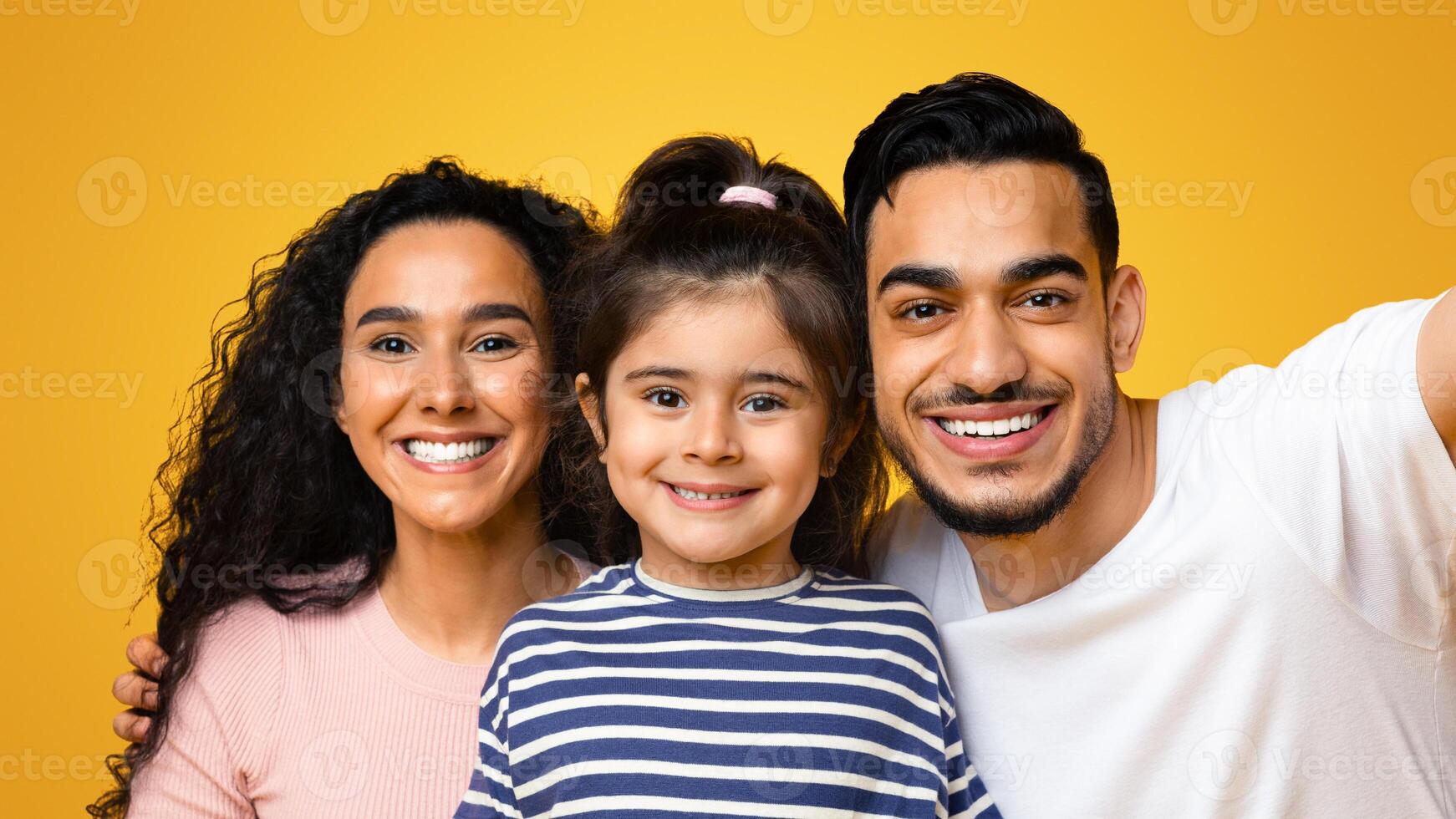 Cheerful Young Middle Eastern Parents And Little Daughter Taking Selfie Together, Happy Arab Family Of Three With Cute Female Child Smiling At Camera While Posing Isolated Over Yellow Background photo