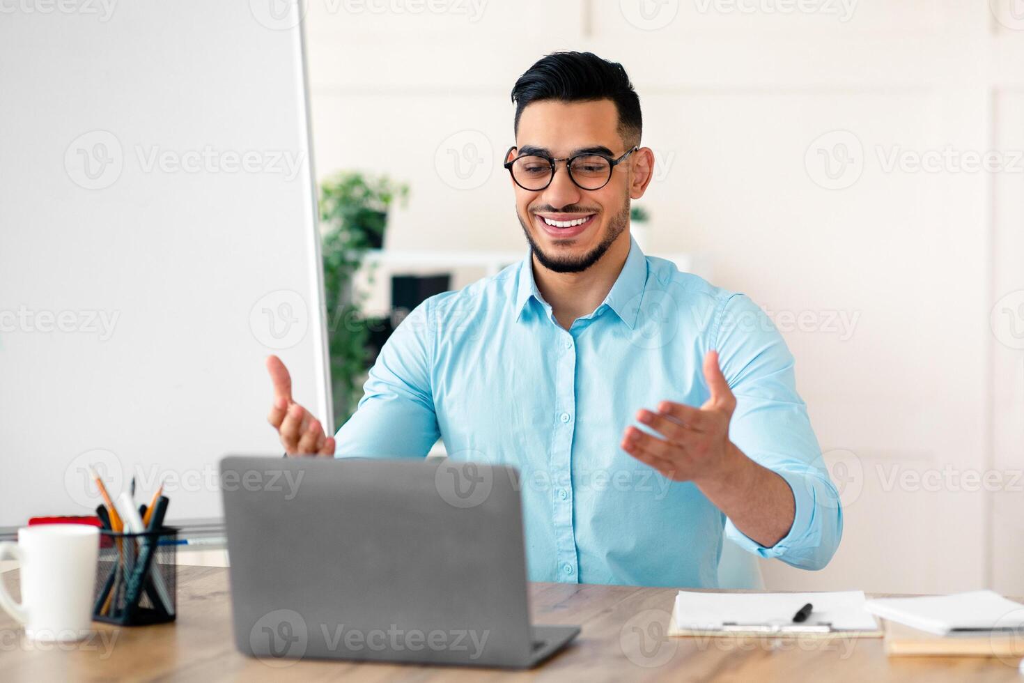 Studying English online. Cheerful Arab guy teacher giving foreign language lesson on web using laptop. Young tutor explaining grammar rules to students on internet during coronavirus lockdown photo