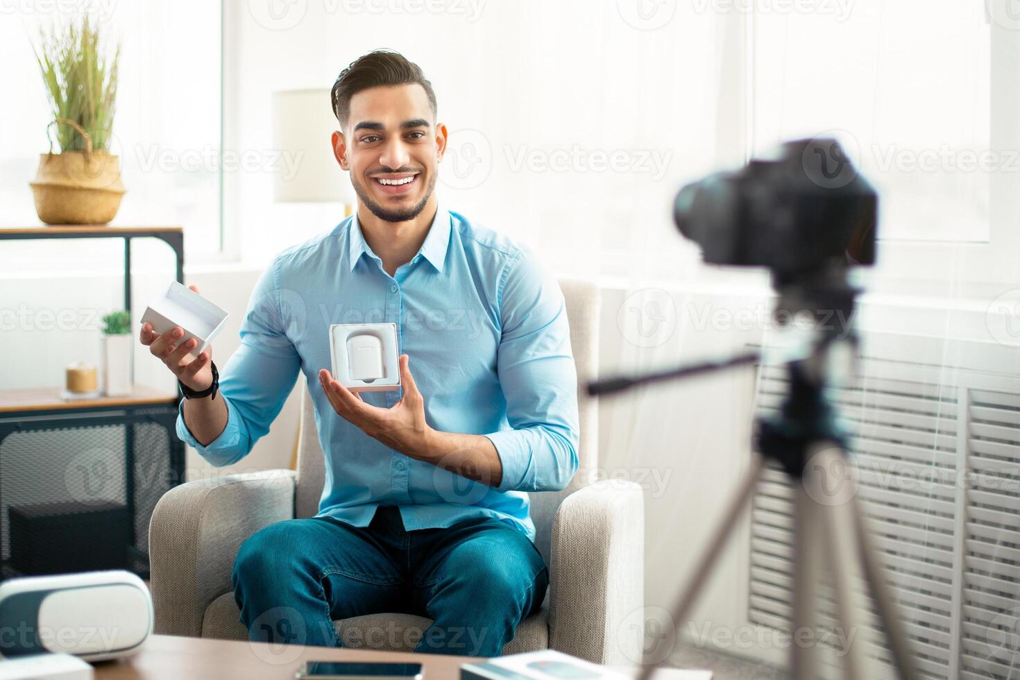 Arab guy vlogger making review of new wireless earphones, using professional camera at home. Famous influencer sharing info about innovative tech product with followers on social network photo
