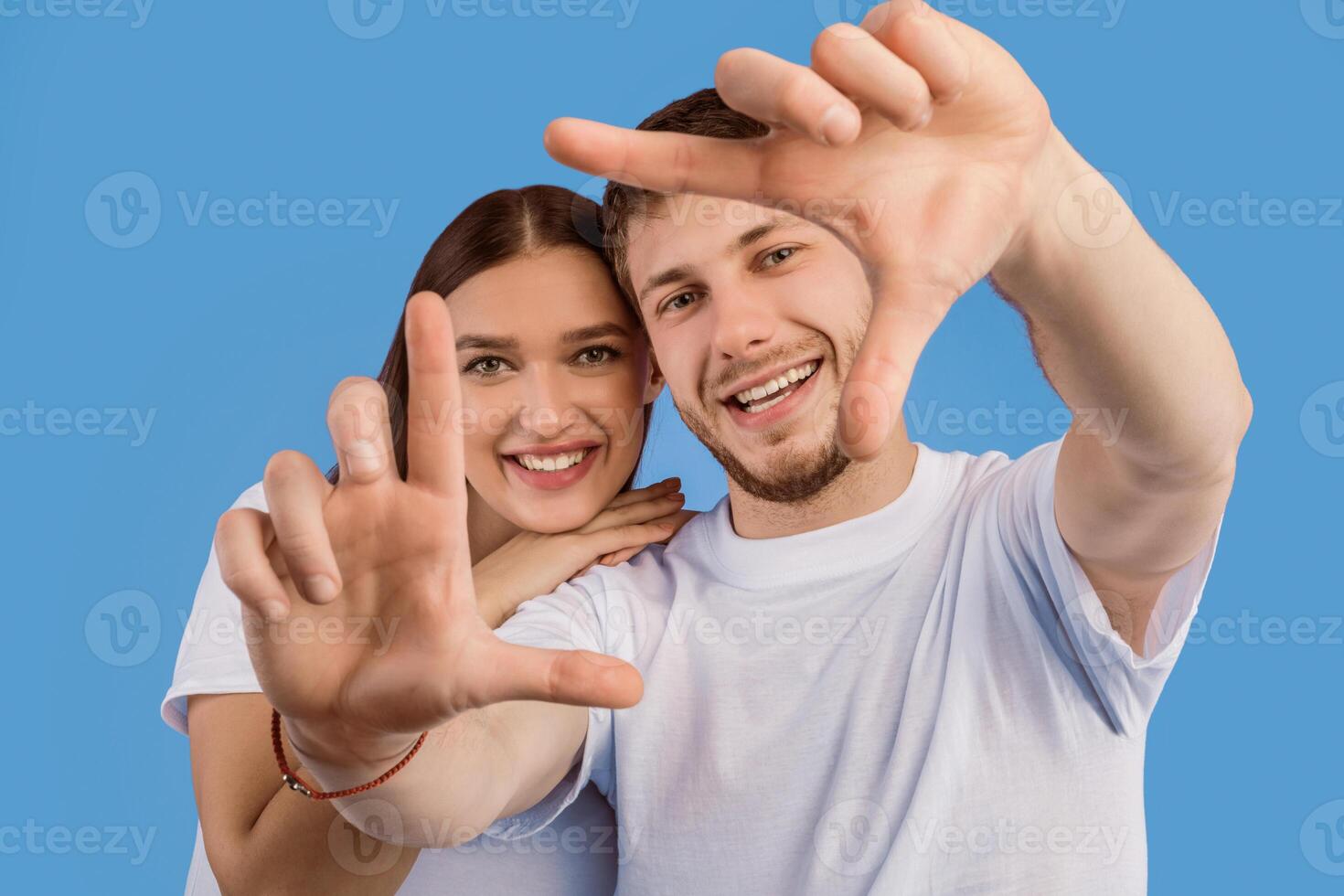 Beautiful young couple making frame, looking at camera and smiling, isolated on purple studio wall photo