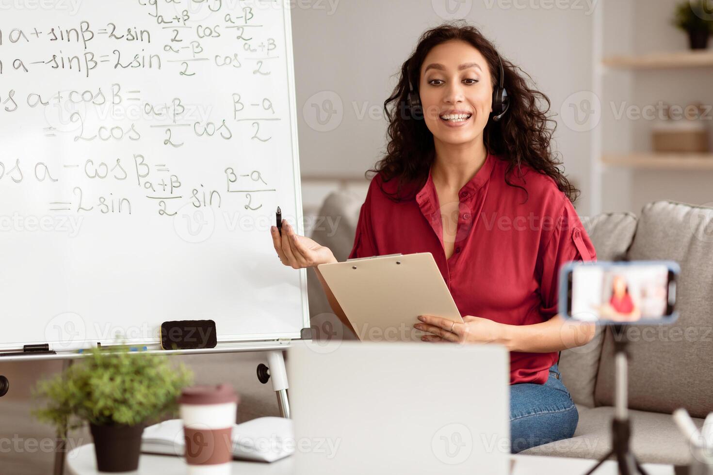 Distance Education Concept. Portrait of lady math teacher explaining trigonometric functions to students making videocall. Lady in headset looking at laptop screen, recording lesson on cellphone photo