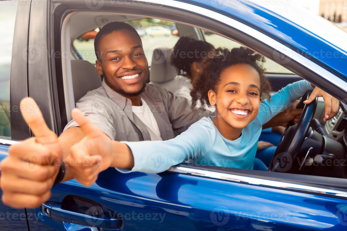 Family Approving New Car. Happy African American Father And Daughter Gesturing Thumbs Up Sitting In Automobile, Smiling To Camera. Road Trip, Transportation. We Like Our Auto. Selective Focus photo