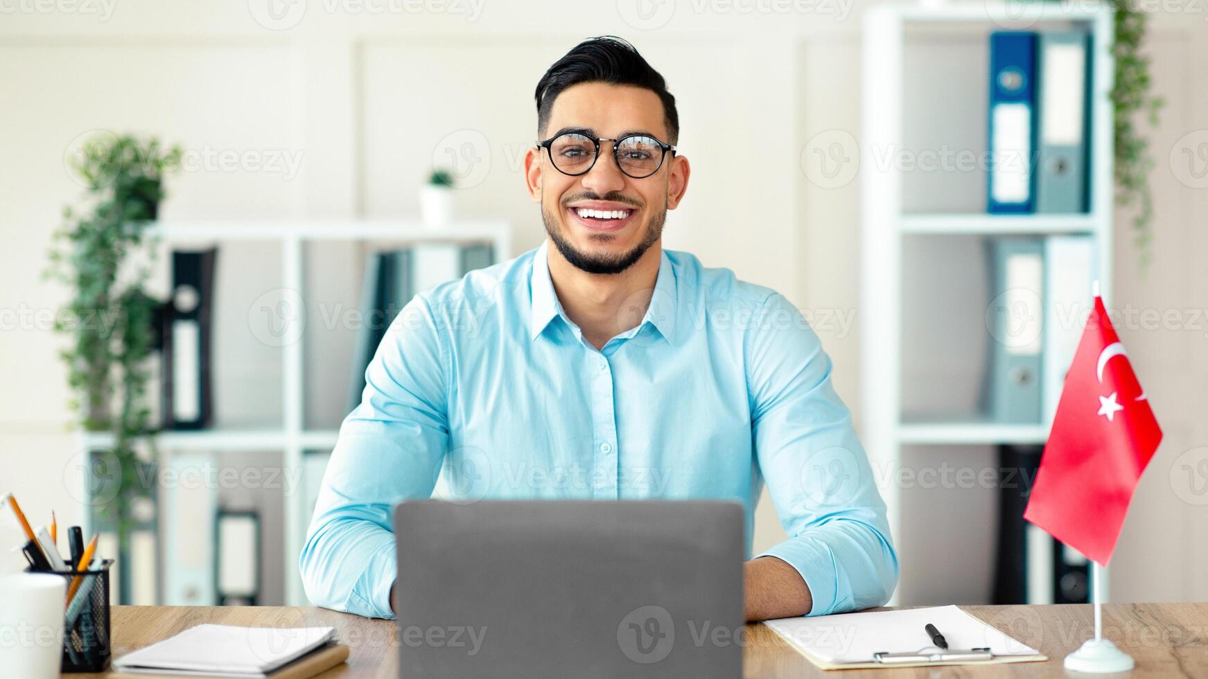 Portrait of millennial guy teacher with laptop teaching Turkish online from home, smiling at camera. Confident Arab guy tutor conducting educational web conference or webinar photo