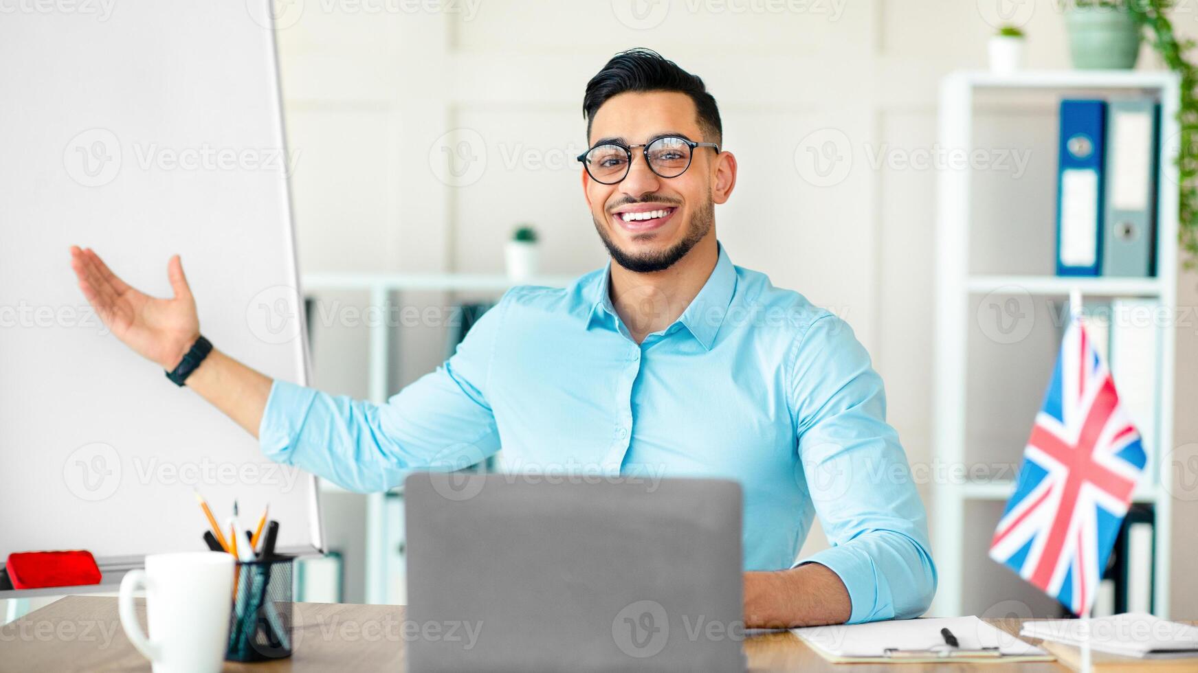 Young Arab tutor teaching British English online, giving foreign language lesson from home office. Guy teacher explaining grammar rules, speaking to remote students on web photo