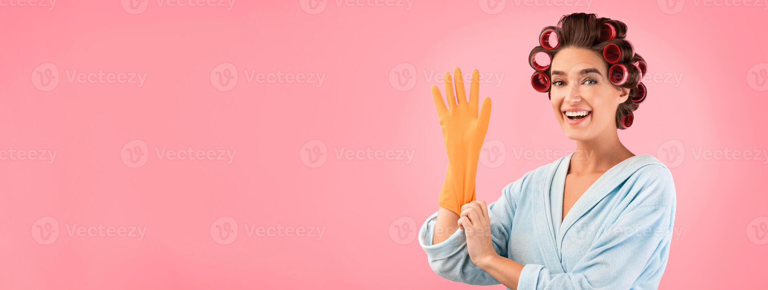 Happy Housewife Putting On Gloves Ready For Spring Cleaning Posing Over Yellow Studio Background. photo
