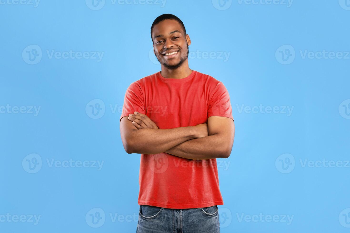Cheerful African American Guy Smiling To Camera Posing Crossing Hands Standing Over Blue Background. Studio Shot Of Happy Self-Confident Black Millennial Man Expressing Positive Emotions photo