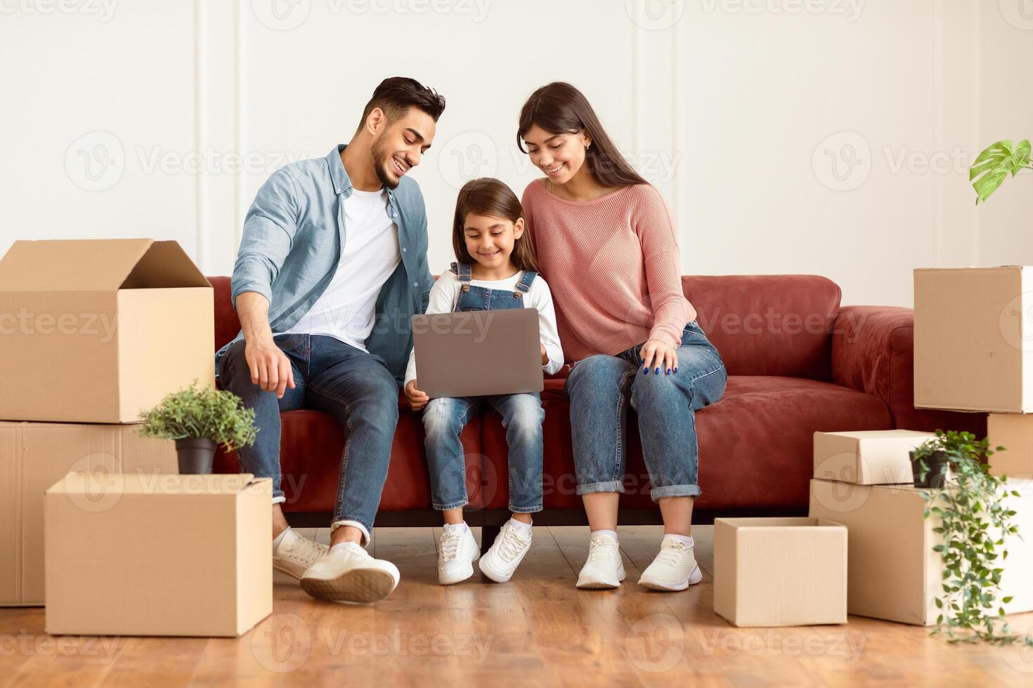 House Ownership And Relocation Project Concept. Portrait Of Happy Young Family Using Laptop Sitting On Couch After Moving New Home. Mom, Dad And Child Browsing Internet, Looking At Screen photo