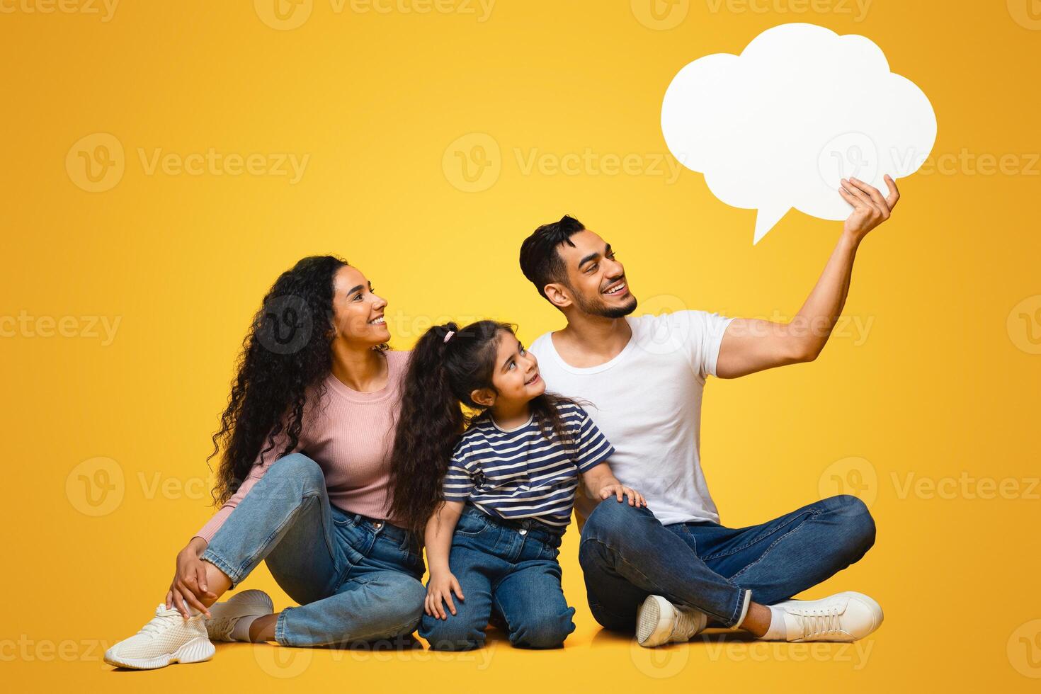 Nice Idea. Happy Arab Family With Little Daughter Looking At Empty Speech Bubble In Father's Hands, Middle Eastern Parents And Child Excited About Interesting Offer, Yellow Background, Copy Space photo