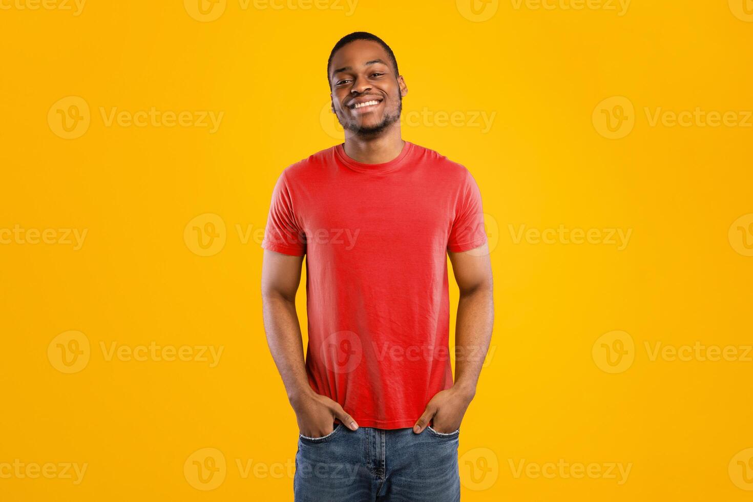 Handsome African American Young Man Posing Holding Hands In Pockets Standing Over Yellow Studio Background. Cheerful Black Man Smiling To Camera Expressing Positive Emotions photo