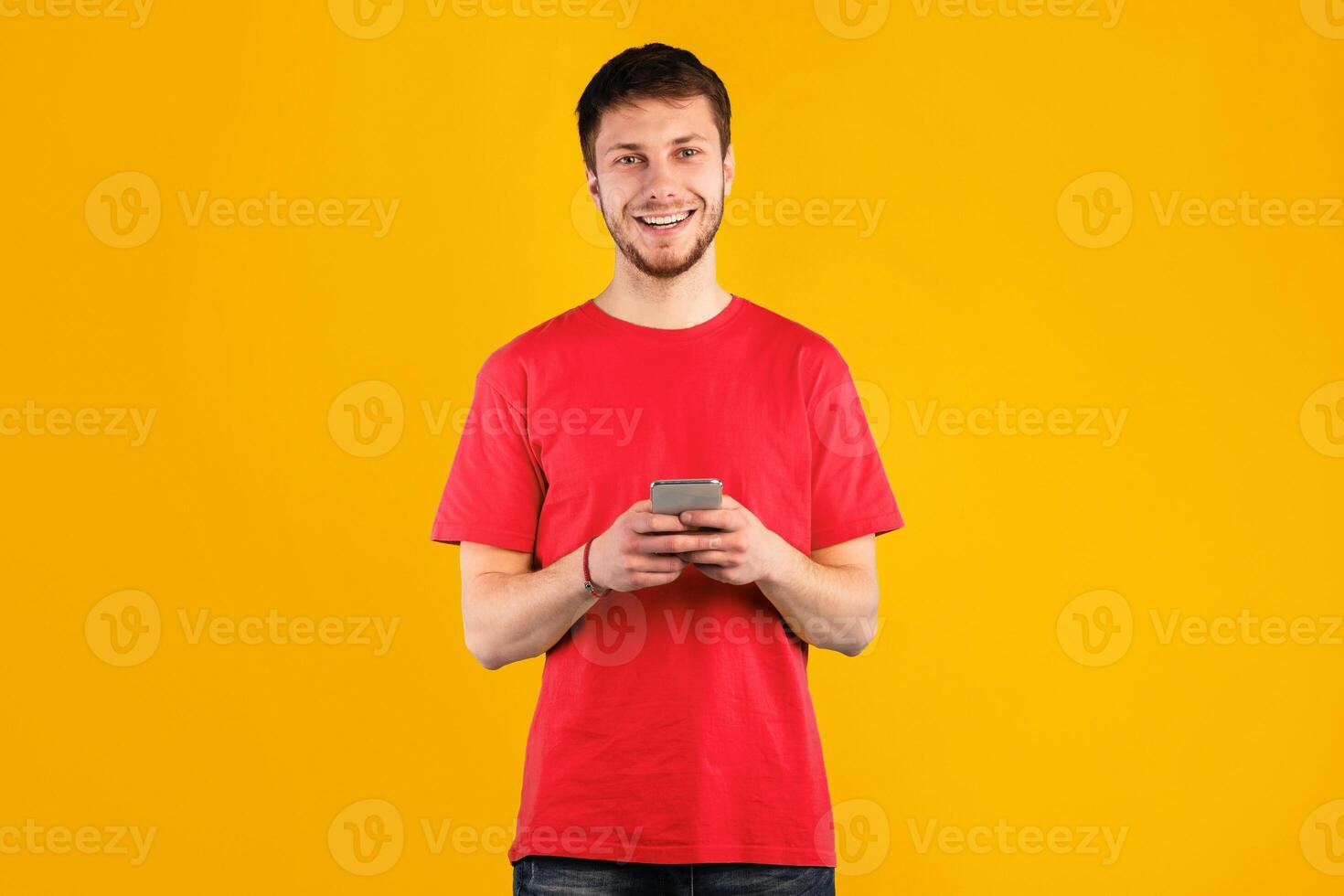 People And Technology Concept. Portrait of happy smiling young man using smartphone standing isolated over blue studio background, copy space. Guy chatting online, looking at camera photo