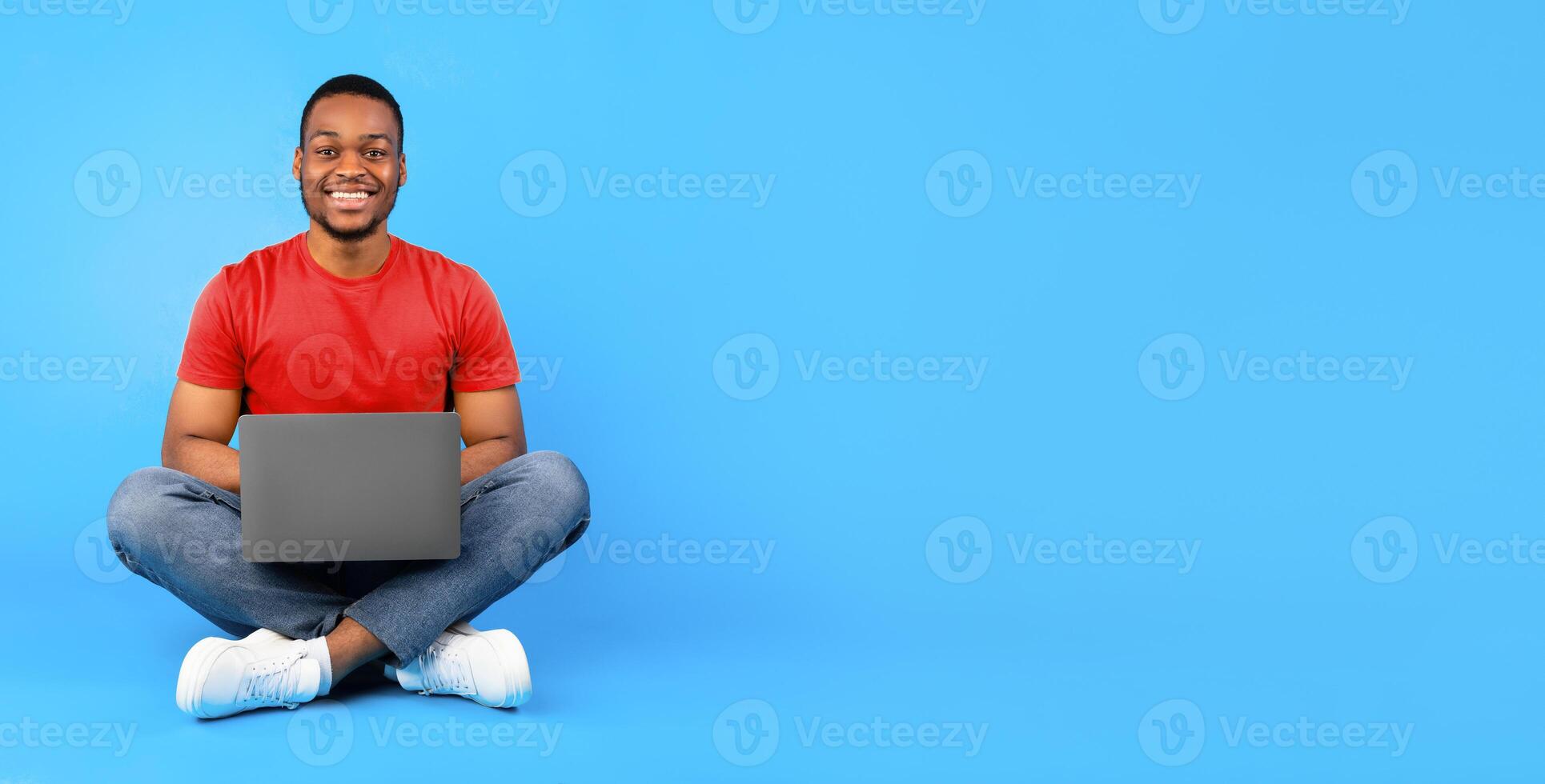 Successful Freelancer Or Blogger. Happy African American Guy Sitting With Laptop Computer Smiling To Camera Posing Over Blue Background. Freelance Career, People And Gadgets, Technology Concept photo