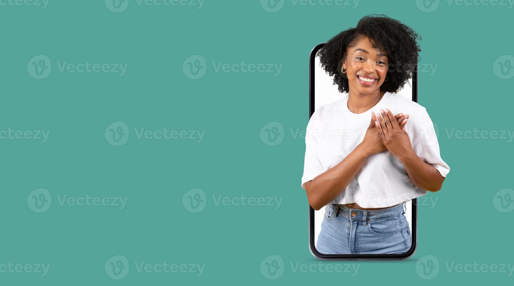 A person with curly hair smiles warmly while interacting with a smartphone. The large screen shows a friendly communication moment. The background is isolated with a solid color. photo