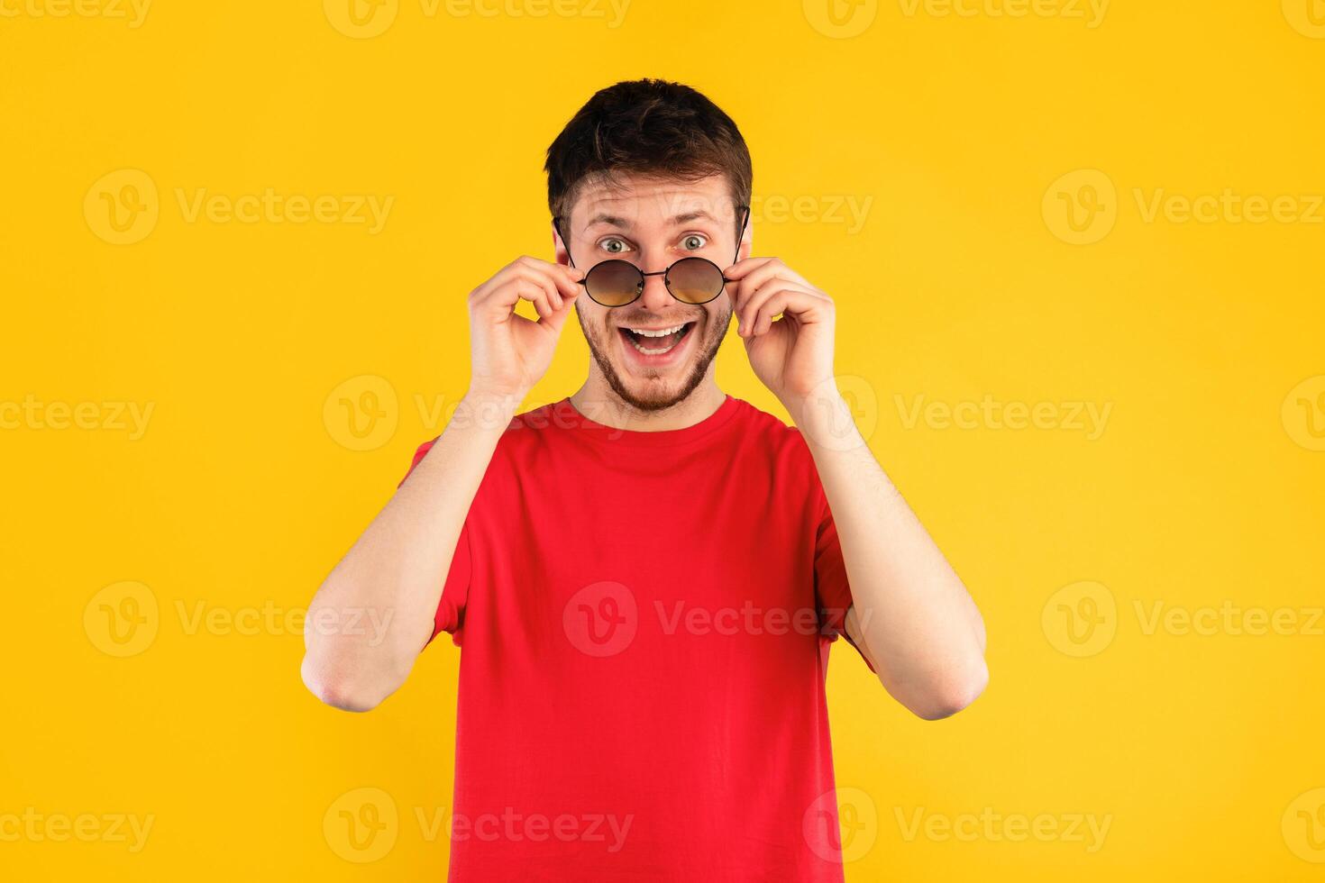 Wow. Portrait of man posing at studio, taking off sunglasses, looking at camera in amazement and with surprised facial expression isolated on blue background. It's Unbelievable. Summer Sale photo
