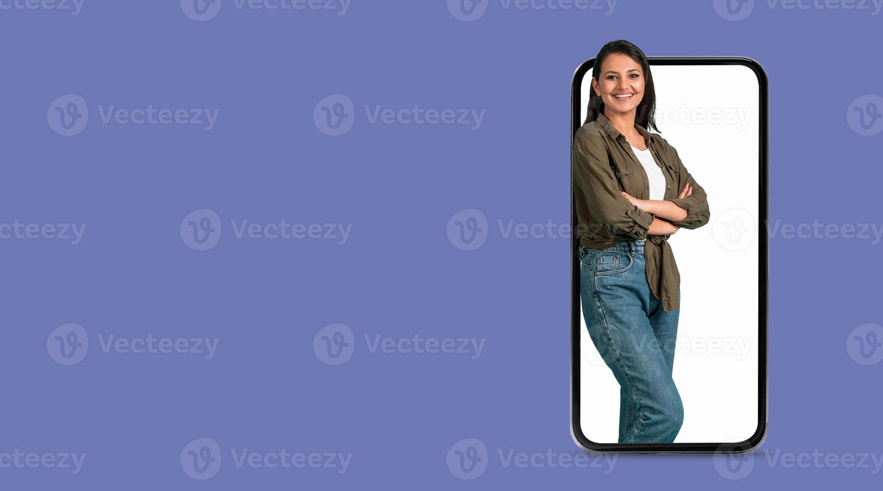 A woman stands confidently while leaning against a large smartphone screen. The person appears engaged, showcasing modern social media usage in a relaxed setting with a plain background. photo