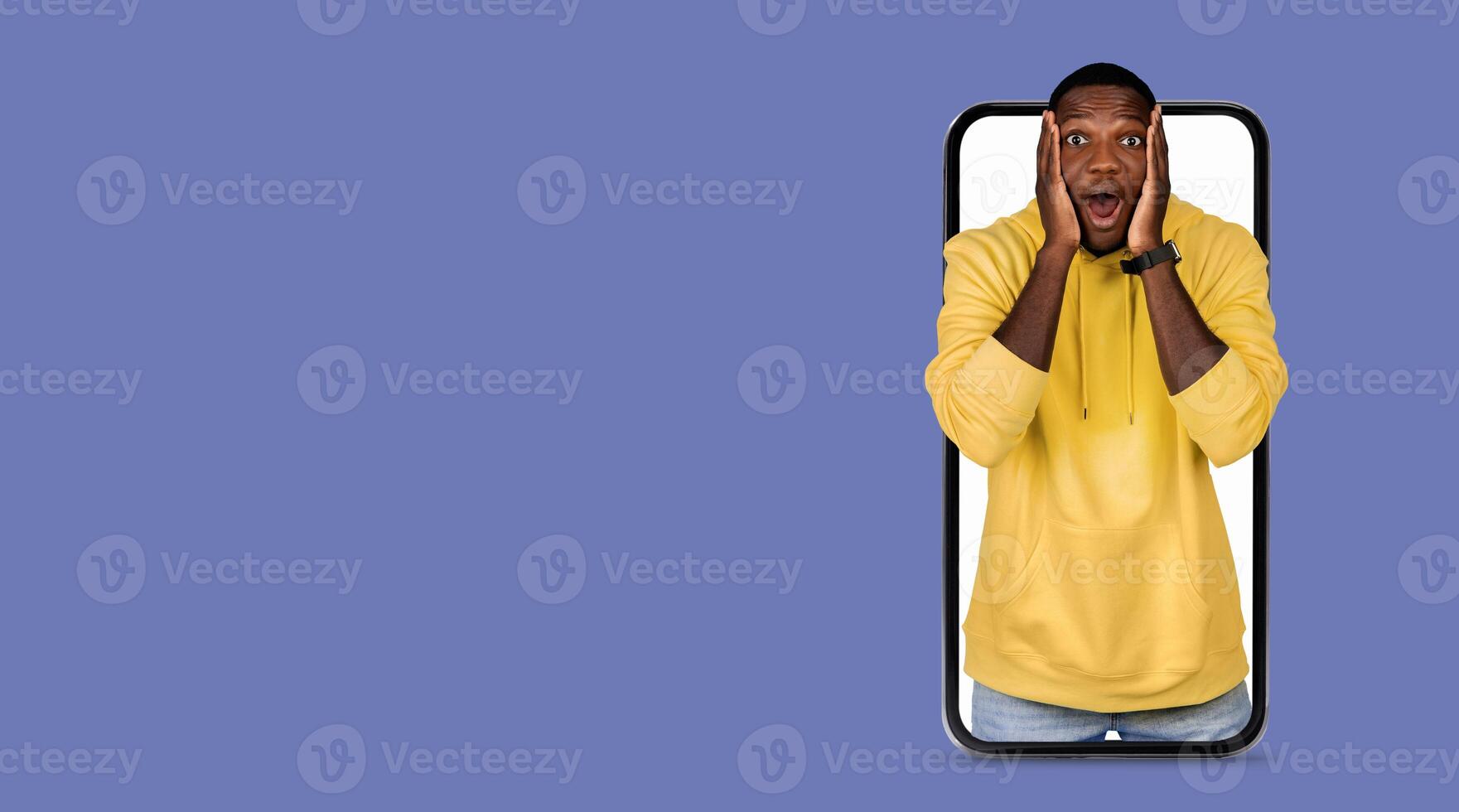 A person in a yellow hoodie shows surprise and joy while using a smartphone with a large screen. The background is a solid color, emphasizing the expression of excitement and the technology in hand. photo
