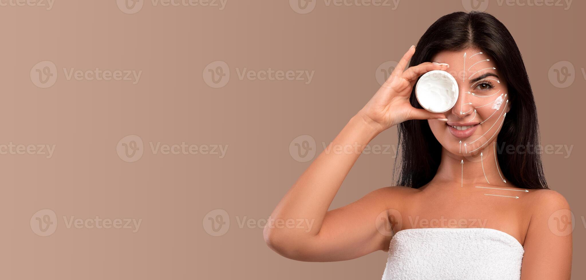 A woman enjoys her skin care routine while holding a jar, ready to apply a treatment. She is isolated against a neutral background, creating a calm and focused atmosphere for her beauty ritual. photo