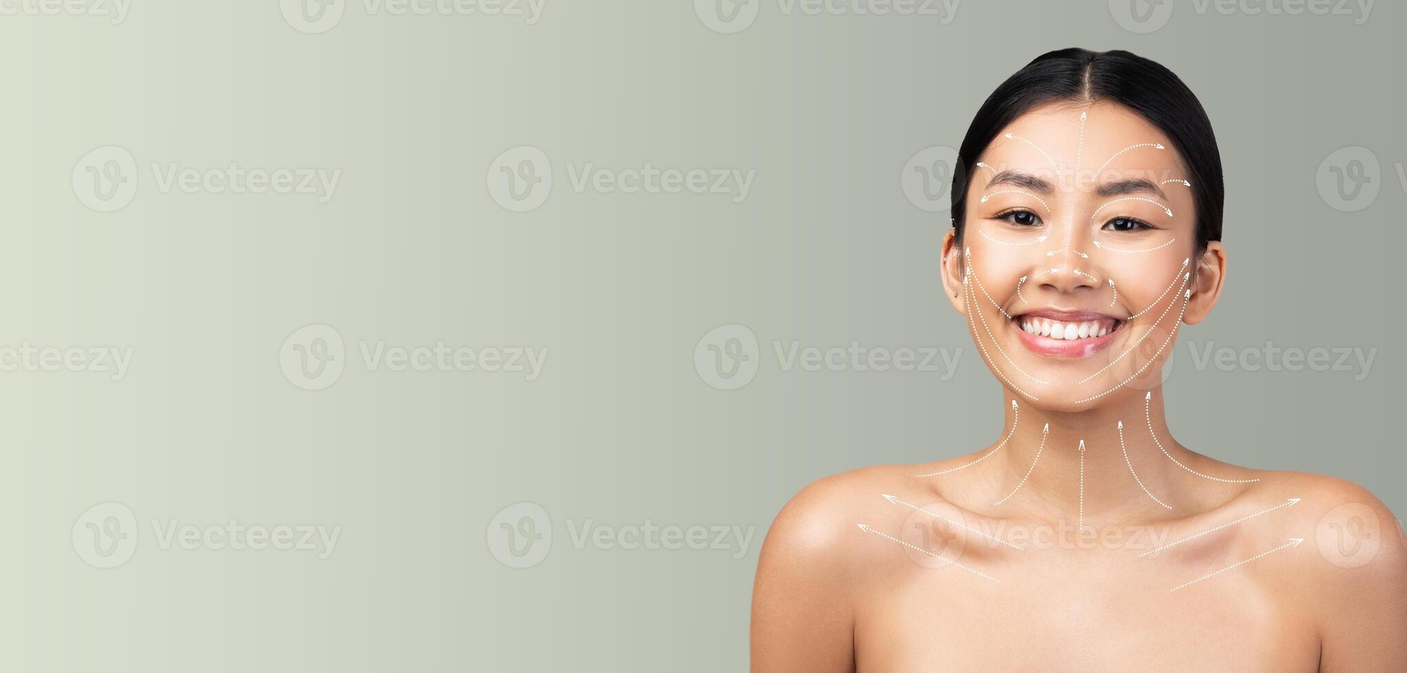 Asian woman stands isolated against a soft background, indulging in her skin care routine. She radiates confidence and happiness while showcasing her pampered skin. photo