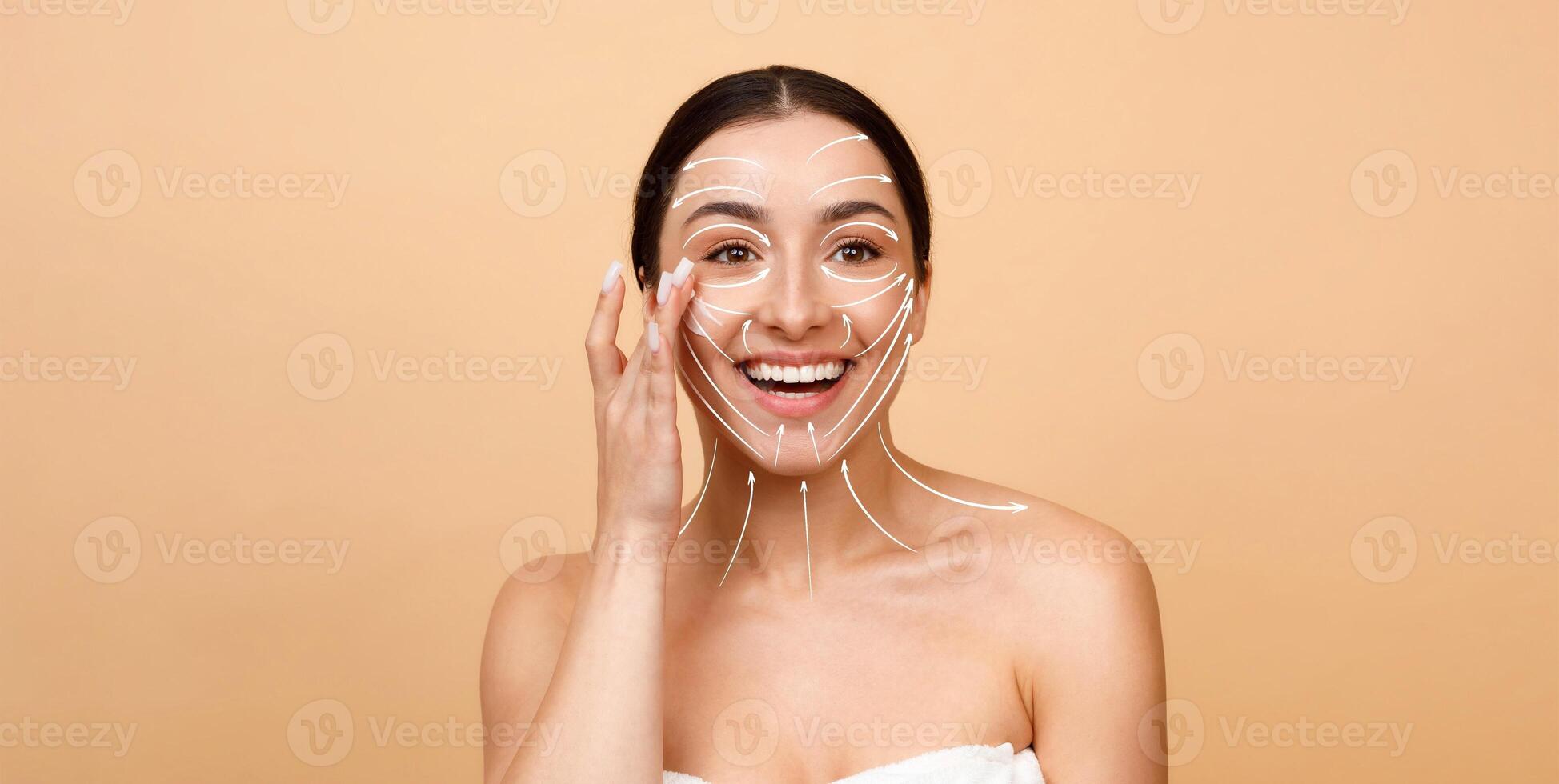 A woman with a radiant smile applies skincare products on her face, showcasing a glow. The setting features an isolated background, emphasizing her beauty and self-care moment. photo