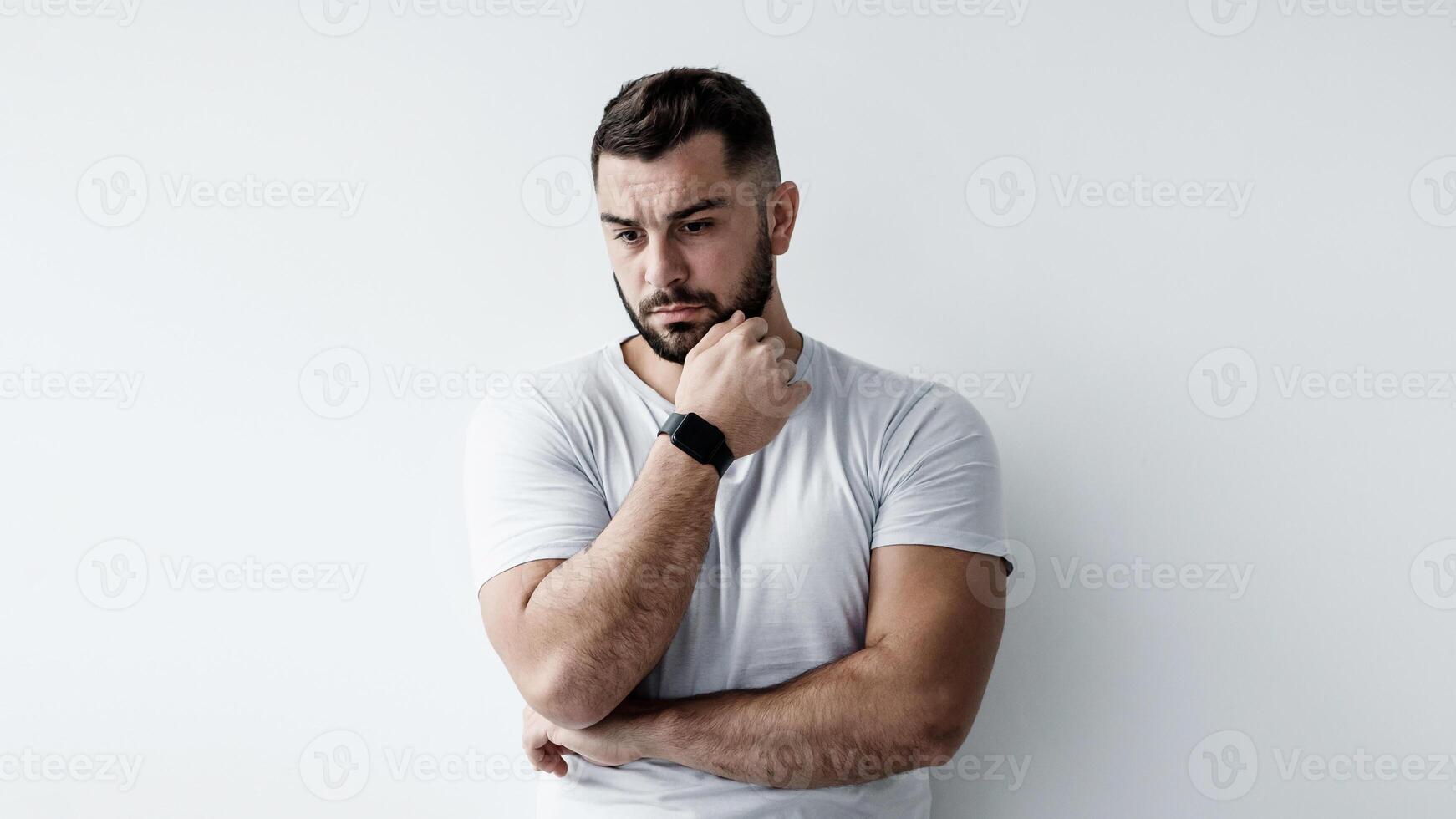 Think, solve problem, negative human emotions, stress and depression. Sad unhappy pensive young european handsome man presses hand to chin and ponders on white wall background, empty space, mockup photo