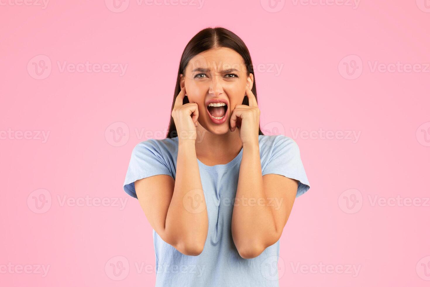 Too loud. Portrait of young annoyed woman closing her ears with fingers, refusing to listen or to hear something, standing isolated over yellow studio background. Lady screaming and shouting photo