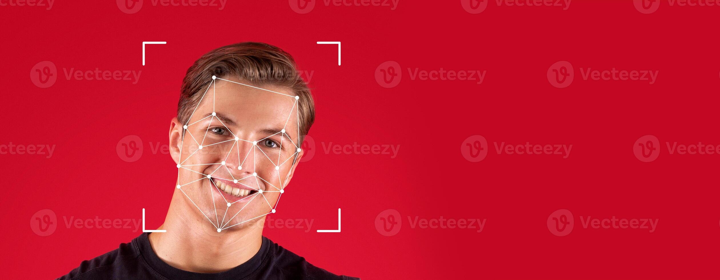 A person smiles while facial recognition technology analyzes their face against a blank red background. This demonstrates the advancements in identification processes in modern society. photo