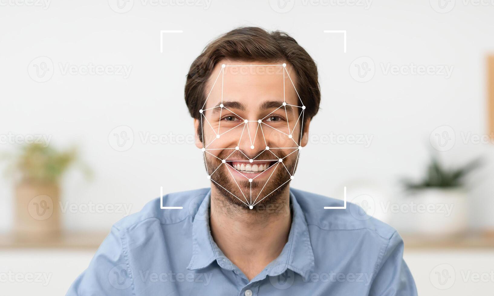 A young man is smiling while facial recognition technology analyzes his features. He is seated in a relaxed environment with greenery visible in the background, indicating a calm atmosphere. photo