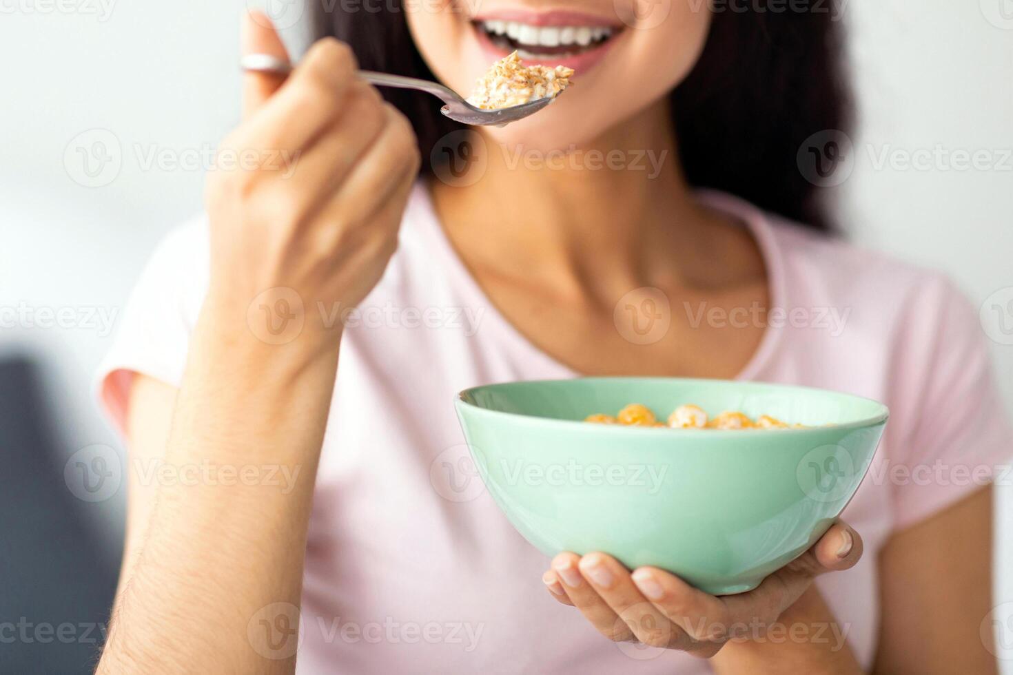 Unrecognizable Indian lady eating cereal from bowl at home, closeup. Cropped view of Hindu woman enjoying cornflakes with milk, having healthy breakfast. Slimming diet concept photo