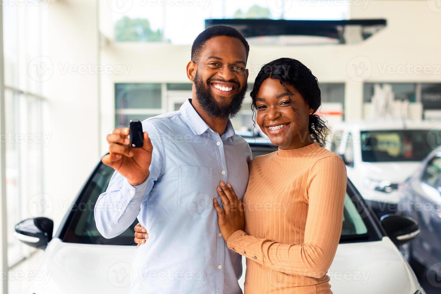 Happy Owners. Cheerful Black Spouses Holding Key Of Their New Car And Smiling At Camera While Posing In Dealership Office, Young African American Couple Buying Automobile In Modern Showroom photo