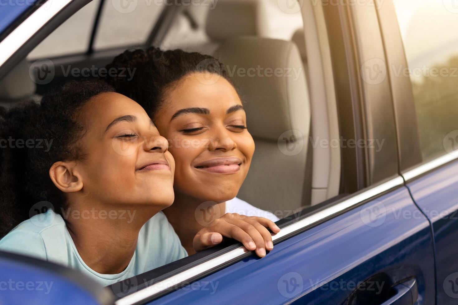 Happy African American Mom And Daughter Sitting In Car Smelling Fresh Air In Opened Window, Enjoying Road Trip Together. Family Traveling By Automobile. Transportation, Vehicle Ownership Concept photo