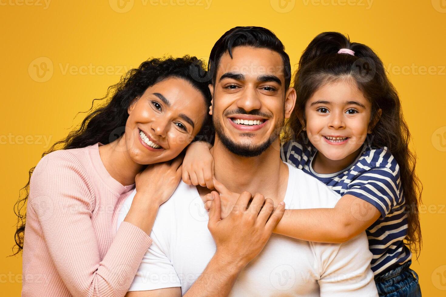 Closeup Portrait Of Happy Middle Eastern Family Of Three With Adorable Little Daughter, Joyful Middle Eastern Parents And Their Cute Female Child Embracing And Posing At Camera Over Yellow Background photo