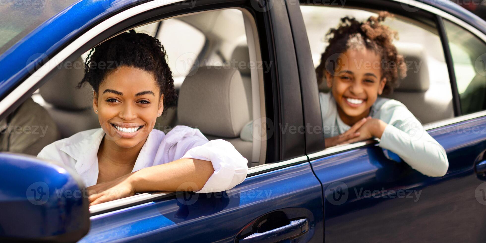 Cheerful Black Mother And Daughter Sitting In New Auto Smiling Looking At Camera Through Opened Car Window. Family Driving Enjoying Road Trip. Selective Focus photo