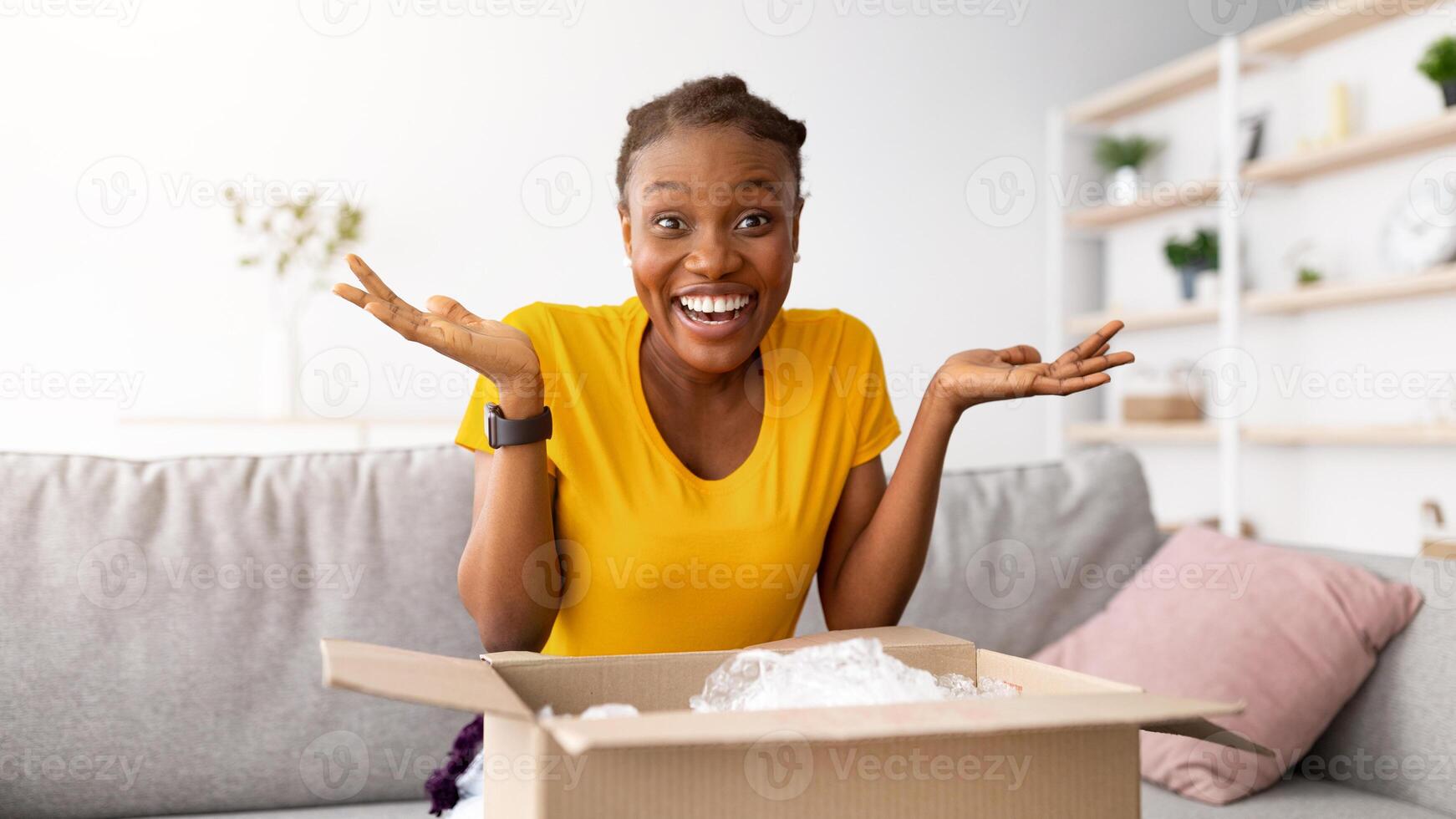 Excited black woman receiving parcel, unpacking cardboard box at home, satisfied with great purchase. Happy African American lady opening carton parcel, overjoyed by online delivery photo