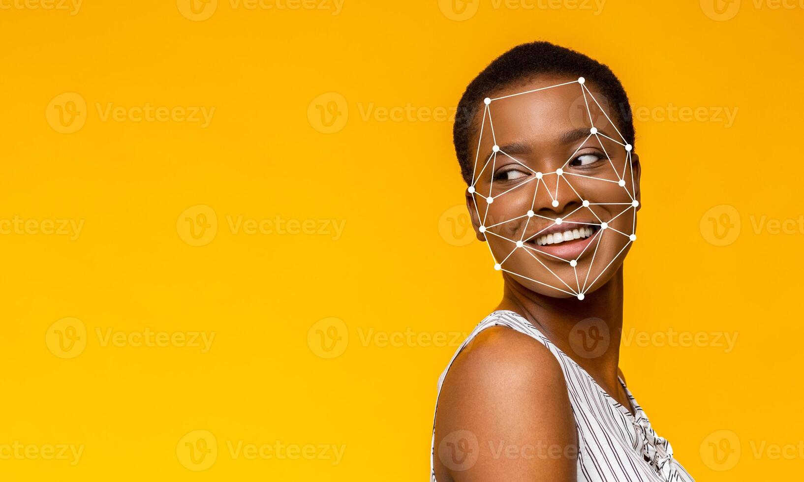 A young woman with a joyful expression turns her head slightly to the side against a vibrant yellow backdrop. Facial recognition points are superimposed on her face, illustrating modern technology. photo