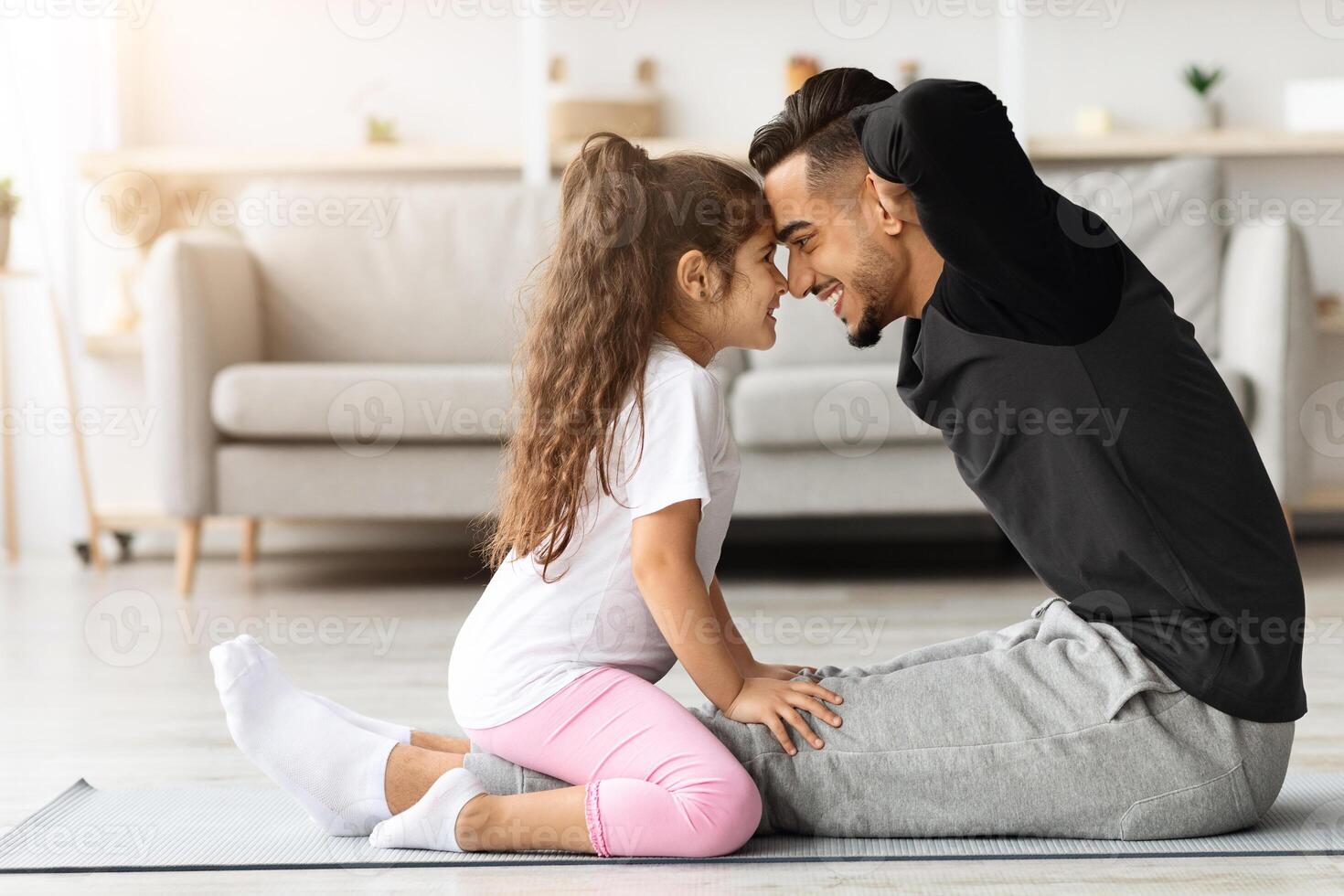 Athletic father and daughter working on abdominal muscles together at home, adorable little girl holding her dad legs while he doing crunches, exercising together in living room, side view, copy space photo