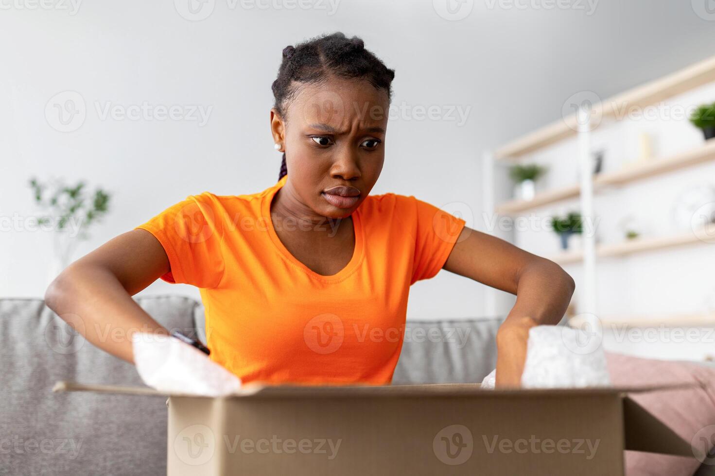 Damaged parcel. Shocked Afro woman unboxing delivery, looking inside wrong box, upset because of shipping mistake, dissatisfied with online shopping service or web store photo
